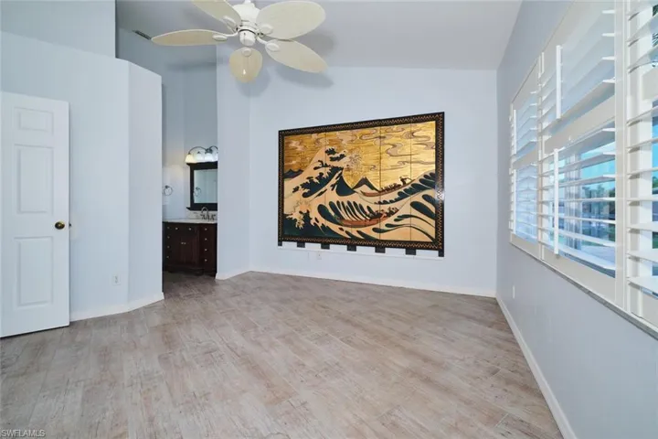 Bedroom with vaulted ceiling, wood-style tile floors, plantation shutters, and a ceiling fan