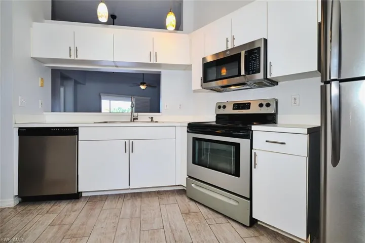 Kitchen featuring stainless steel appliances, light "looks like wood" tile finished floors, white cabinets, and pendant lighting