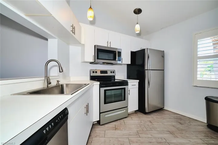 Kitchen featuring stainless steel appliances, light countertops, white cabinets, decorative light fixtures, and plantation shutters.