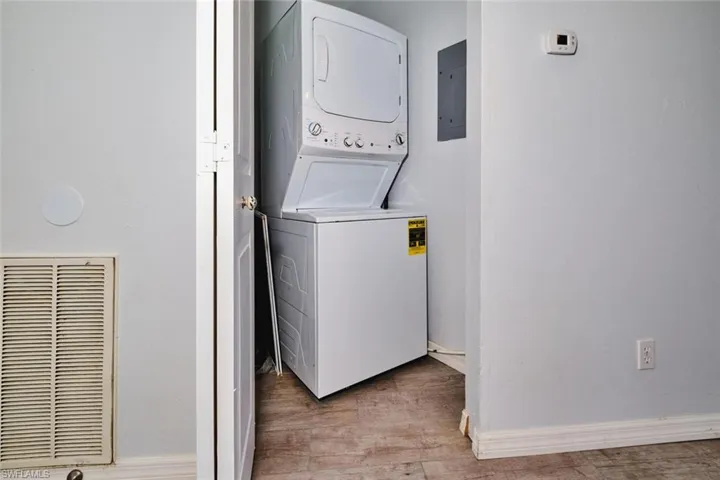 Washroom featuring stacked washer / dryer, light wood-style tile floors, and water heater.