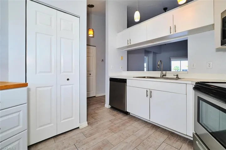 Kitchen featuring stainless steel appliances, light countertops, white cabinets, decorative light fixtures, and plantation shutters, pantry closet.