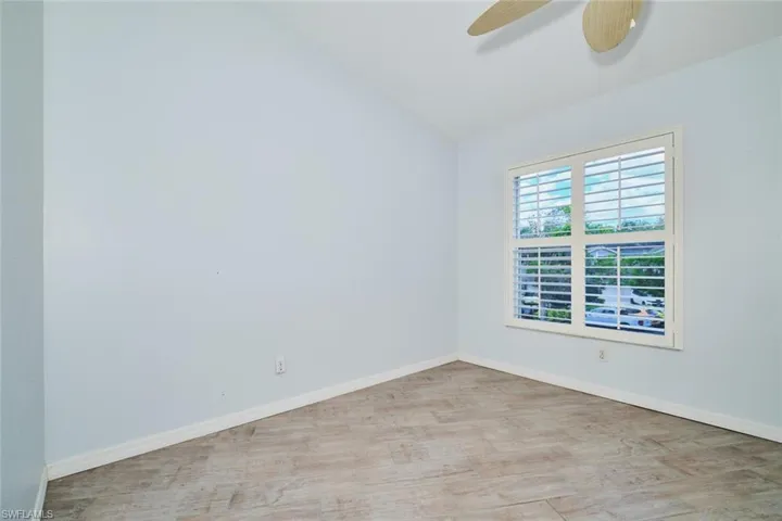 Guest bedroom with lofted ceiling, light wood-like tile floors, plantation shutters and ceiling fan