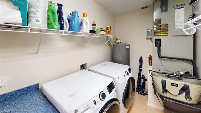 Laundry room with washer and clothes dryer, electric water heater, and light tile patterned floors