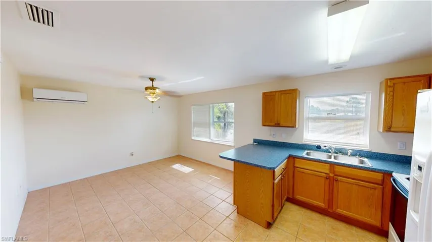 Kitchen with sink, white appliances, ceiling fan, a wall unit AC, and kitchen peninsula