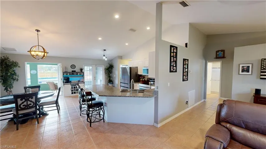 Kitchen with a breakfast bar, hanging light fixtures, stainless steel appliances, light stone countertops, and white cabinets