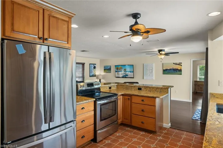 Kitchen featuring light stone countertops, ceiling fan, stainless steel appliances, dark hardwood / wood-style flooring, and kitchen peninsula