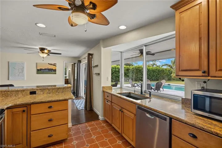 Kitchen with light stone counters, sink, stainless steel appliances, and dark tile patterned flooring