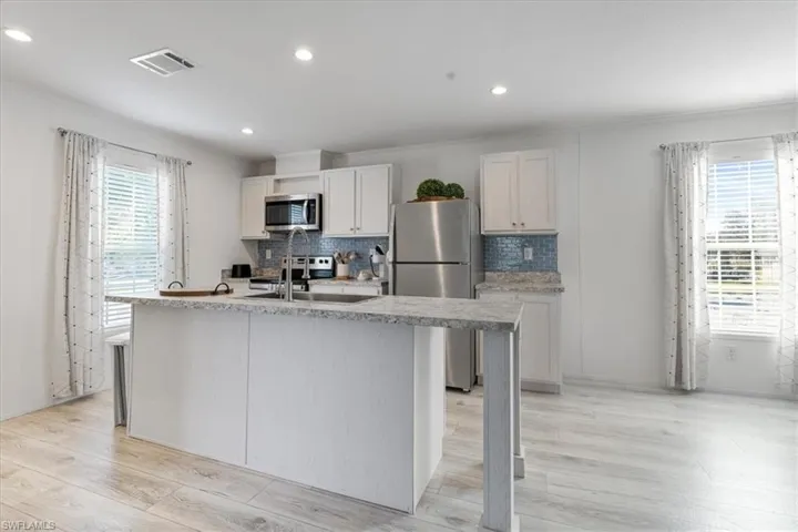 Kitchen featuring stainless steel appliances, white cabinetry, sink, and a center island with sink
