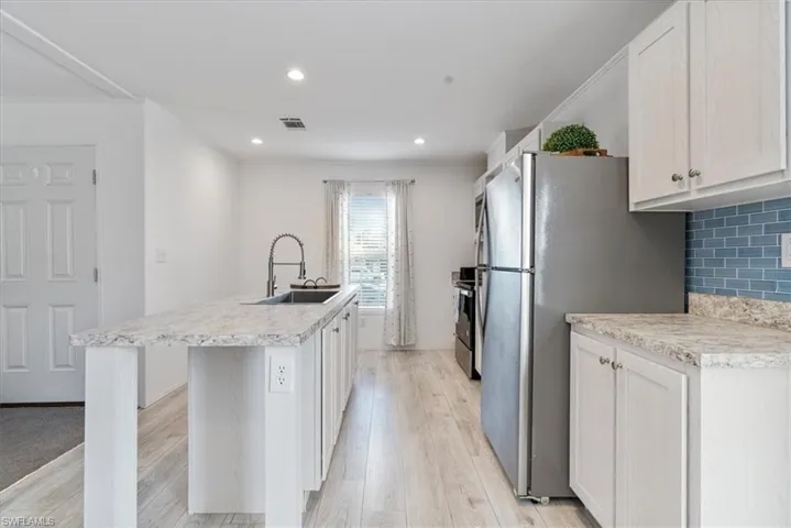 Kitchen with sink, a center island with sink, white cabinets, and decorative backsplash
