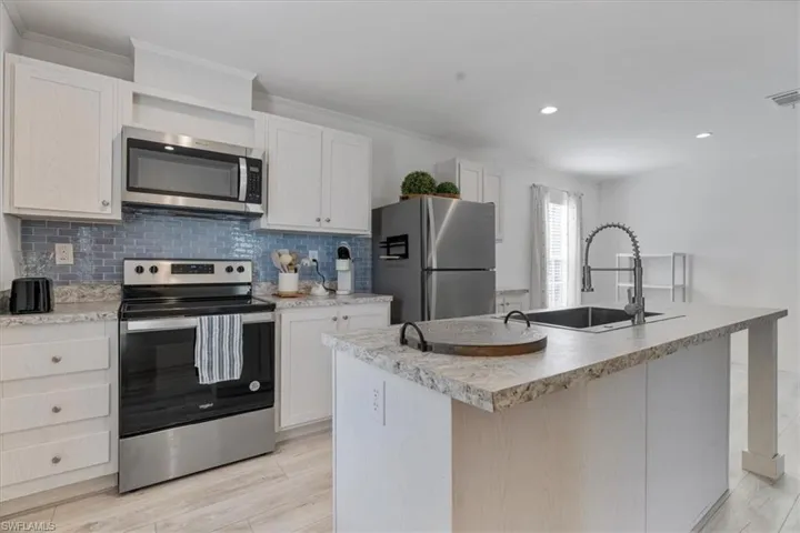 Kitchen with tasteful backsplash, appliances with stainless steel finishes, a center island with sink, and white cabinets