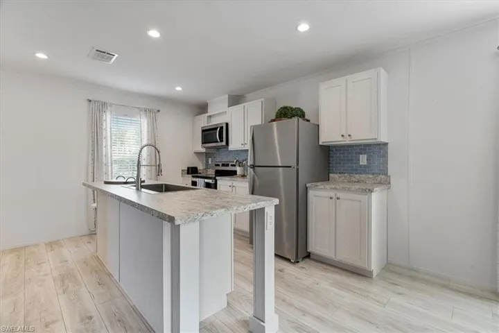 Kitchen featuring sink, white cabinetry, stainless steel appliances, light hardwood / wood-style floors, and an island with sink