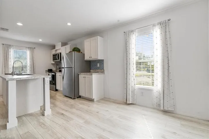 Kitchen featuring sink, light hardwood / wood-style flooring, a center island with sink, appliances with stainless steel finishes, and white cabinets
