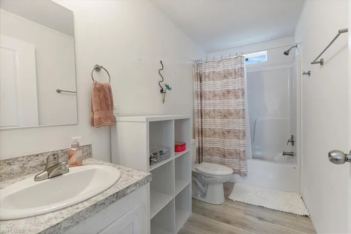 Full bathroom with shower / bathtub combination with curtain, vanity, hardwood / wood-style flooring, and toilet