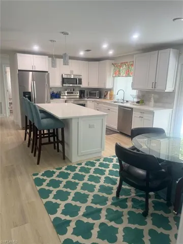 Kitchen with light wood finished floors, appliances with stainless steel finishes, light countertops, a center island, and white cabinets