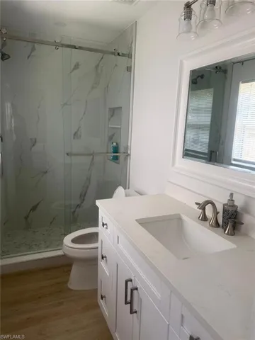Full bathroom featuring vanity, a marble finish shower, and wood finished floors