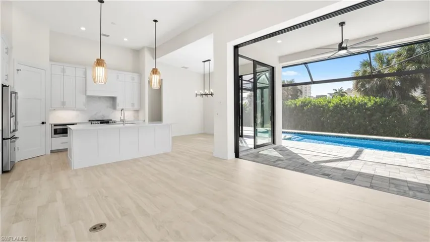 Kitchen with white cabinetry, a center island with sink, pendant lighting, freestanding refrigerator, and light wood finished floors