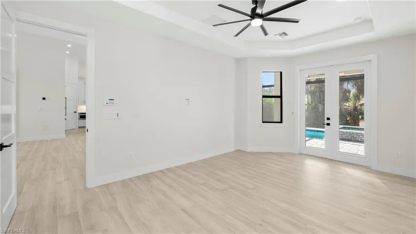 Empty room with french doors, light wood-style flooring, ceiling fan, recessed lighting, and a raised ceiling