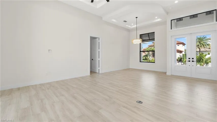 Empty room featuring french doors, a high tray ceiling, light wood-type flooring, and recessed lighting