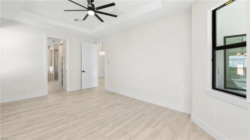 Unfurnished bedroom featuring light wood-type flooring, ceiling fan, and a tray ceiling