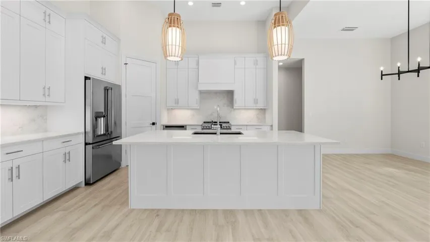 Kitchen featuring high end fridge, light stone countertops, light wood-style floors, white cabinets, and pendant lighting