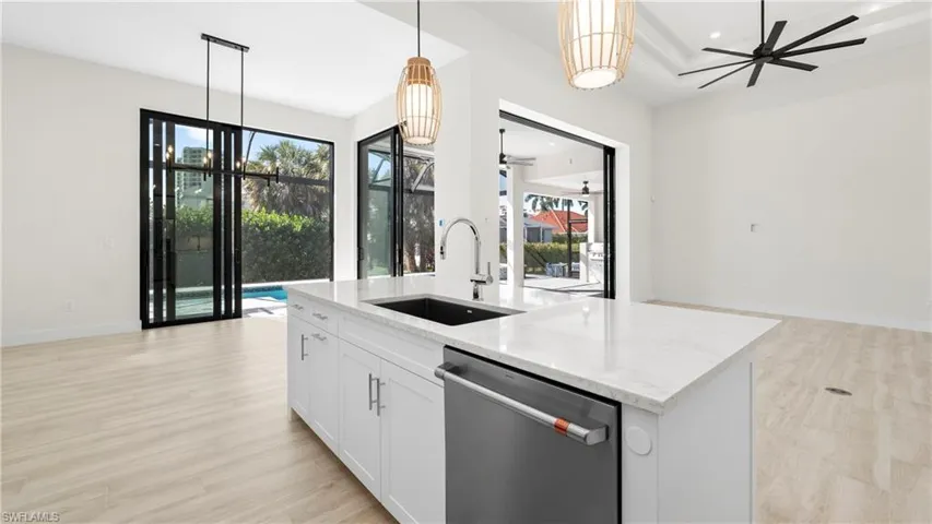 Kitchen featuring ceiling fan, stainless steel dishwasher, light stone counters, an island with sink, and light wood-style floors