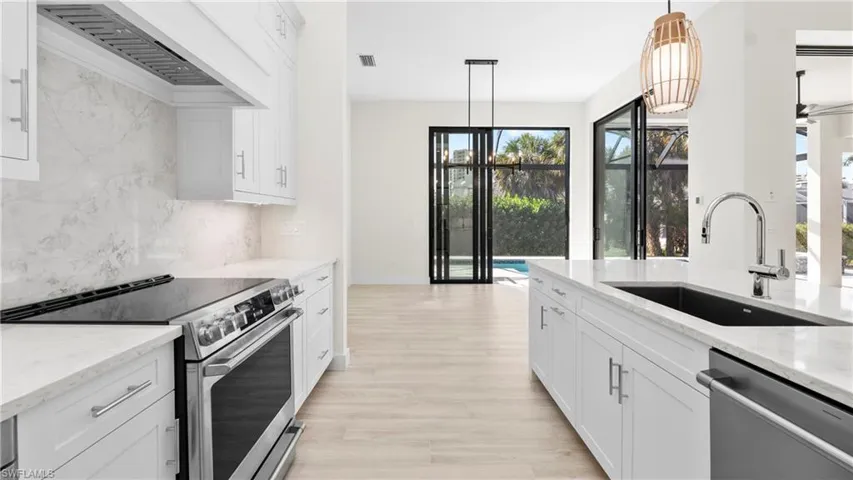 Kitchen featuring stainless steel appliances, white cabinetry, light stone counters, light wood-type flooring, and backsplash