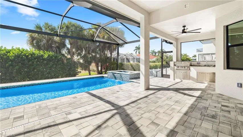 Combined pool / hot tub featuring exterior kitchen, a patio area, a sunroom, and glass enclosure