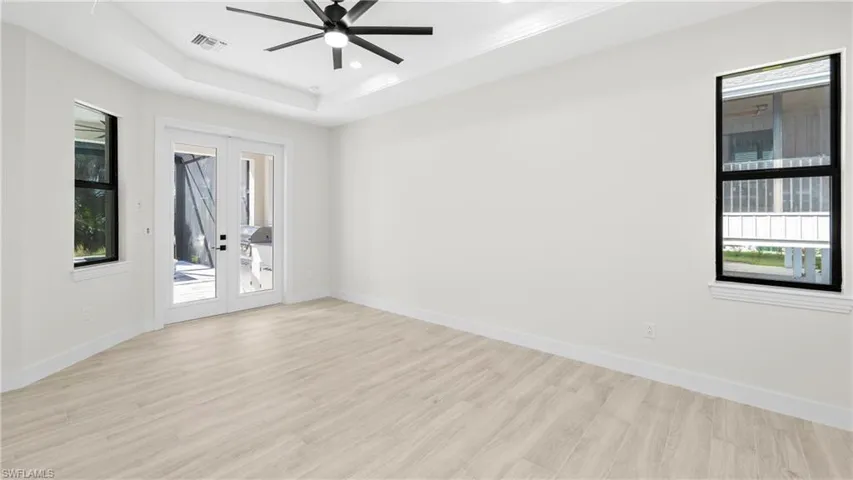 Empty room with french doors, light wood finished floors, ceiling fan, a raised ceiling, and crown molding