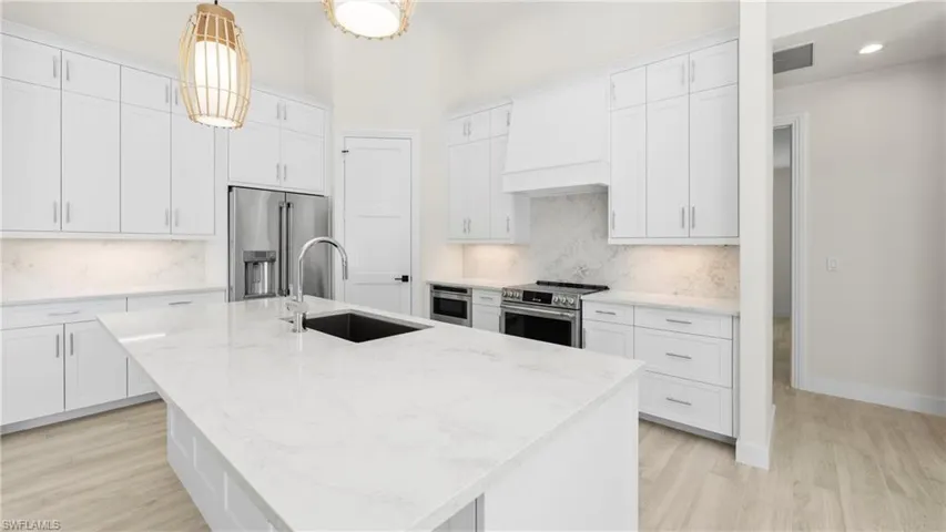 Kitchen with a center island with sink, stainless steel appliances, white cabinetry, light stone countertops, and light wood-type flooring