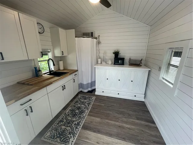Kitchen featuring white cabinets, butcher block countertops, lofted ceiling, wood walls, and dark wood-type flooring