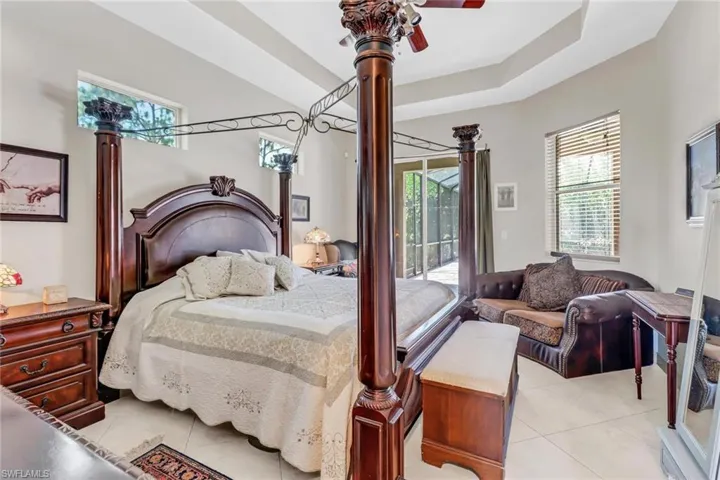 Tiled bedroom with ceiling fan, a raised ceiling, and access to outside