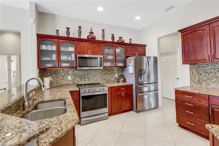 Kitchen with sink, stainless steel appliances, tasteful backsplash, light stone counters, and light tile patterned flooring