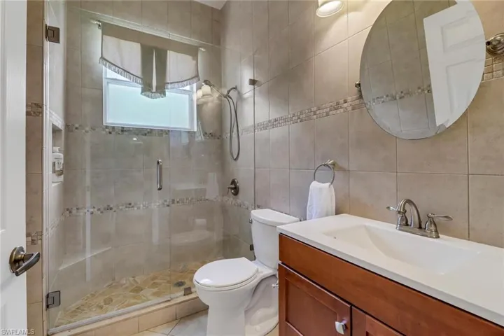 Bathroom with toilet, an enclosed shower, tasteful backsplash, tile walls, and vanity