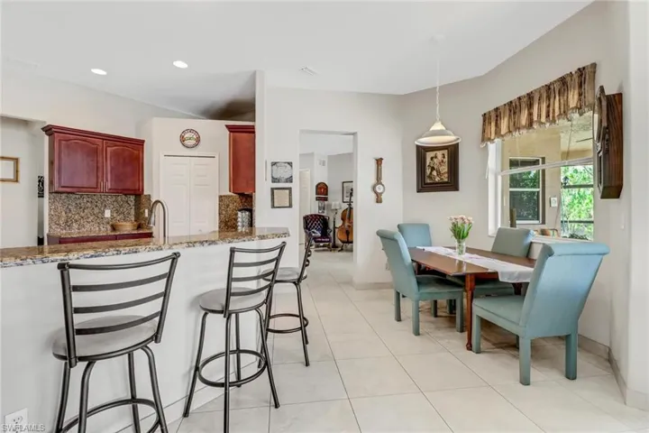 Kitchen featuring pendant lighting, light tile patterned floors, a breakfast bar area, light stone counters, and tasteful backsplash