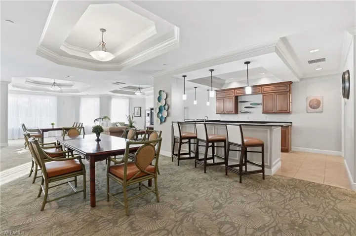 Community room featuring a raised ceiling, ornamental molding, light colored carpet, and light tile patterned floors - Virtually Edited Image