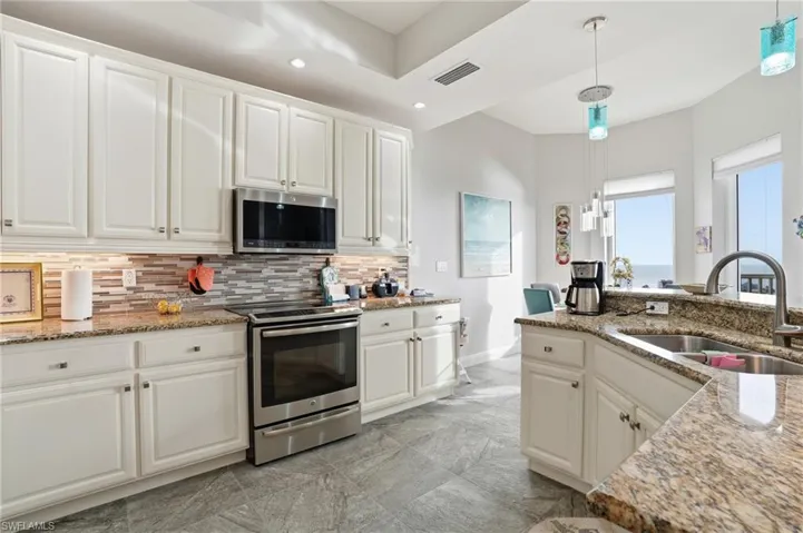 Kitchen with white cabinetry, light stone countertops, stainless steel appliances, hanging light fixtures, and recessed lighting - Virtually Edited Image