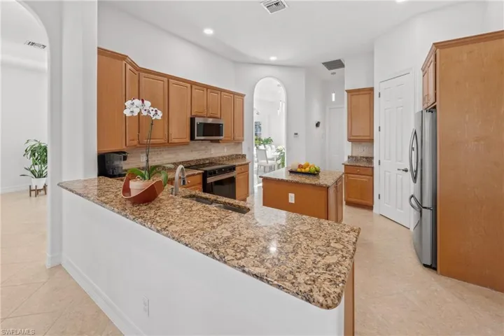 Kitchen with a sink, backsplash, light stone countertops, appliances with stainless steel finishes, and arched walkways