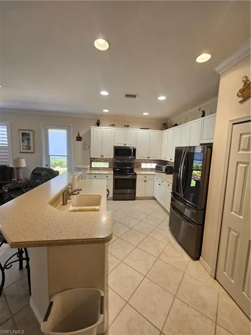 Kitchen featuring stainless steel appliances, ornamental molding, white cabinetry, an island with sink, and recessed lighting