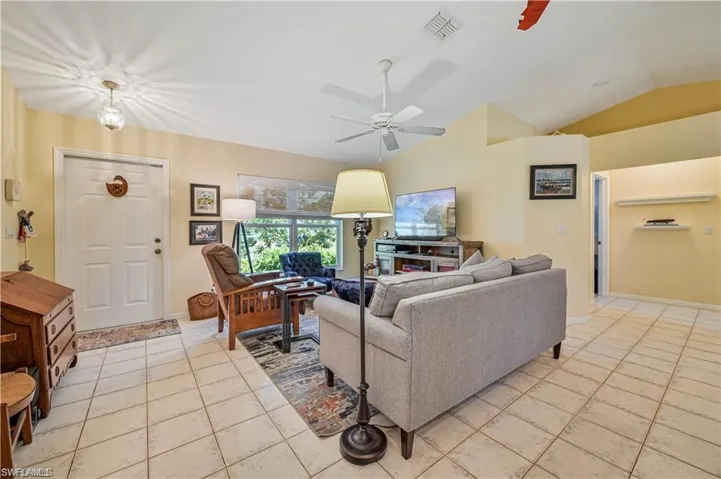 Living room with light tile patterned floors, ceiling fan, and lofted ceiling