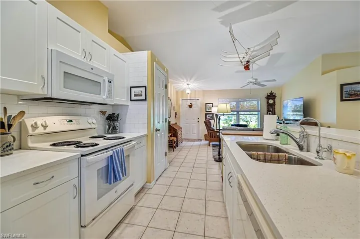 Kitchen with ceiling fan, sink, white cabinetry, vaulted ceiling, and white appliances