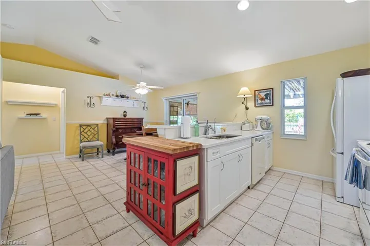Kitchen with lofted ceiling, white appliances, sink, ceiling fan, and white cabinetry