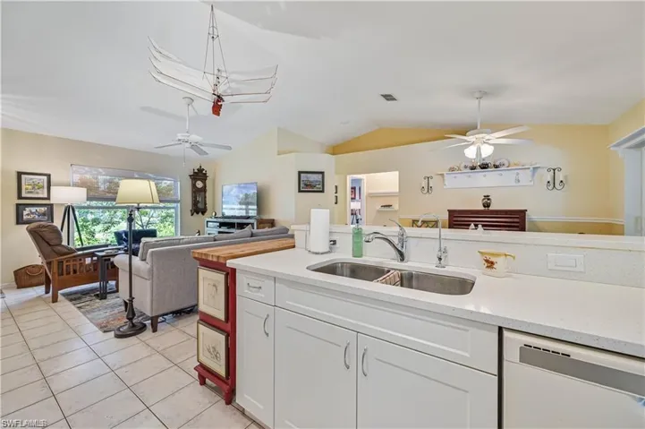 Kitchen featuring sink, light tile patterned floors, white dishwasher, lofted ceiling, and white cabinets