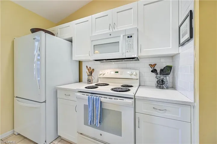 Kitchen featuring backsplash, white appliances, vaulted ceiling, white cabinets, and light tile patterned flooring
