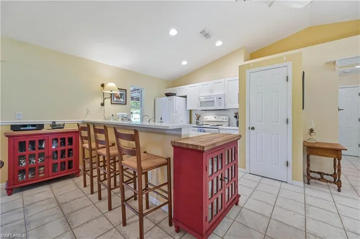 Kitchen with butcher block counters, white cabinetry, a kitchen breakfast bar, lofted ceiling, and white appliances