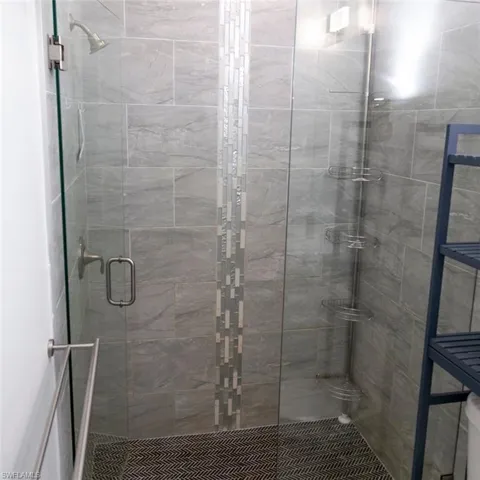 Shower enclosure featuring a glass door with a brushed nickel handle, gray rectangular wall tiles, and a vertical mosaic accent strip