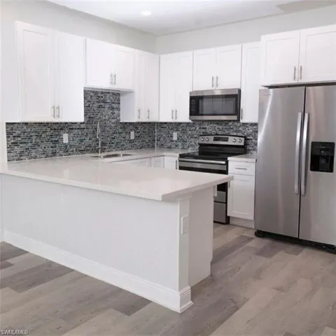 Modern kitchen featuring white shaker cabinetry, stainless steel appliances, a mosaic tile backsplash, light-toned countertops, and wood-finish flooring