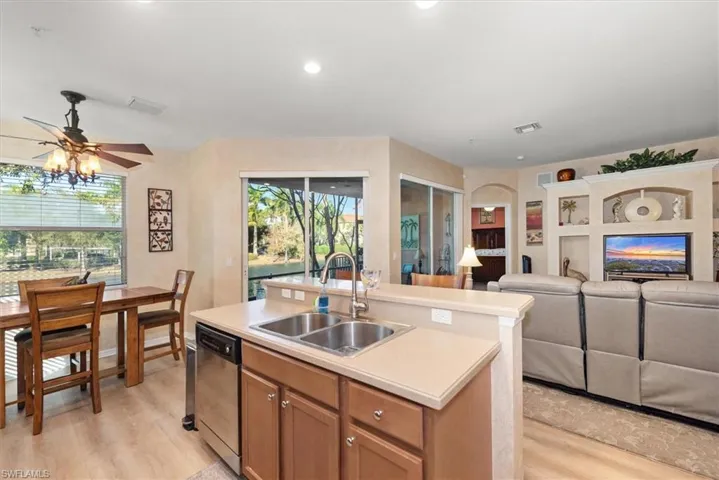 Kitchen with an island with sink, light countertops, brown cabinets, stainless steel dishwasher, and open floor plan