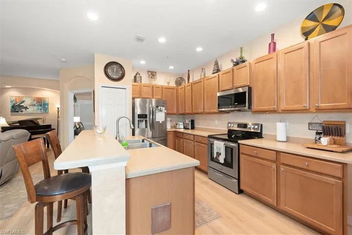 Kitchen featuring appliances with stainless steel finishes, a kitchen bar, light countertops, open floor plan, and a center island with sink