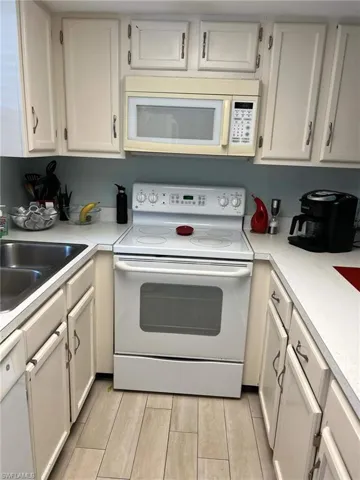 Kitchen with white appliances, light countertops, wood tiled floors, and white cabinetry
