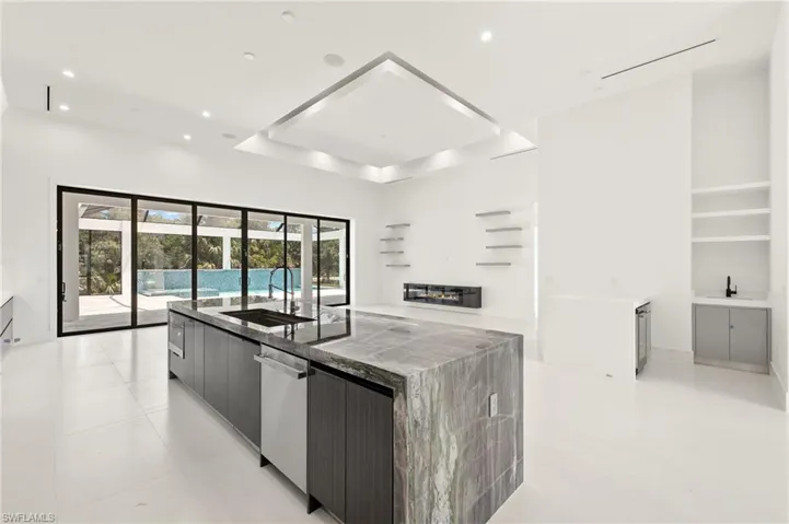Kitchen with a tray ceiling, stainless steel dishwasher, an island with sink, light tile floors, and sink